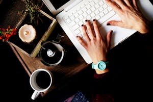 Top view of hands typing on a laptop with a coffee cup on a wooden table.